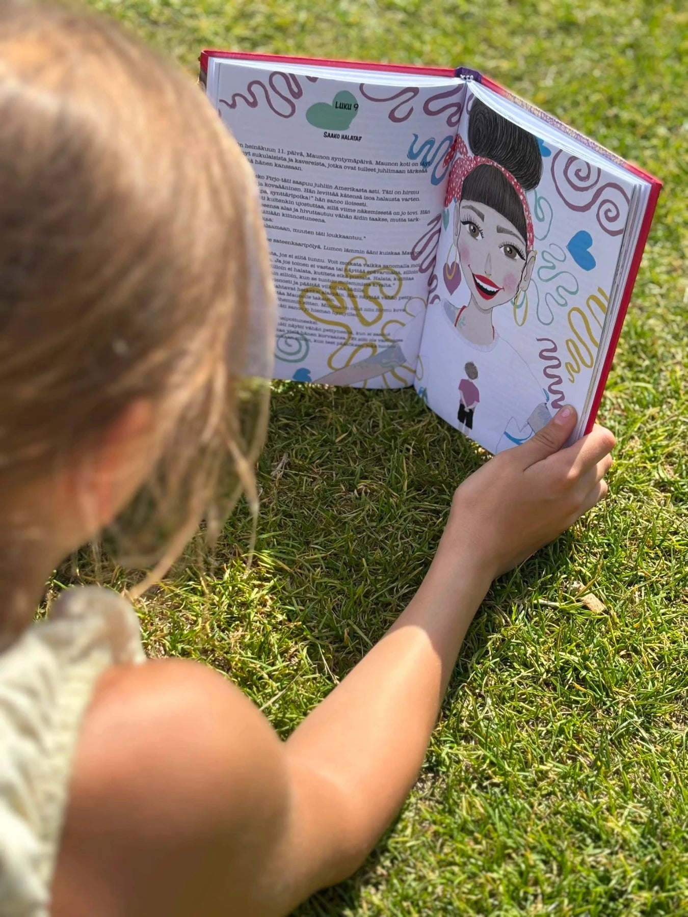 Lapsi lukee nurmikolla kirjailija Jenni Hirvensalon Ei!-Maailman tärkein pieni sana -kuvakirjaa, jonka aukeamalla Sonja Ahosen kuvituskuva.